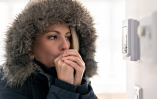 woman in a coat warming her hands looking at the thermostat